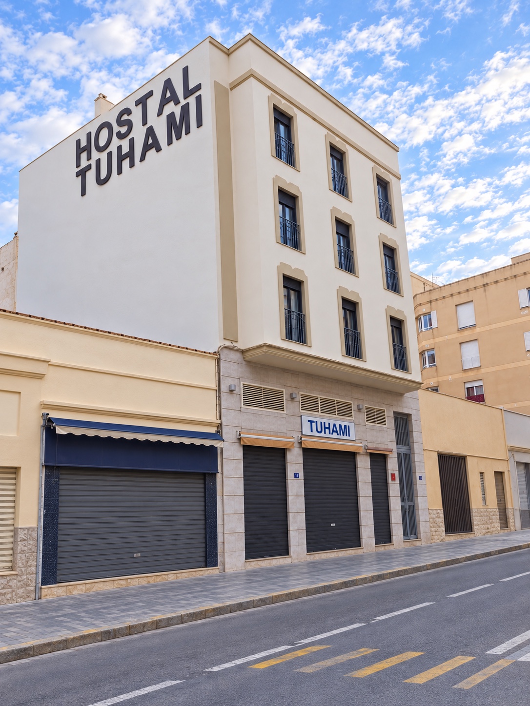 Perspectiva lateral despejada de Hostal Tuhami en Melilla, con el rótulo del hostal, balcones y persianas azules