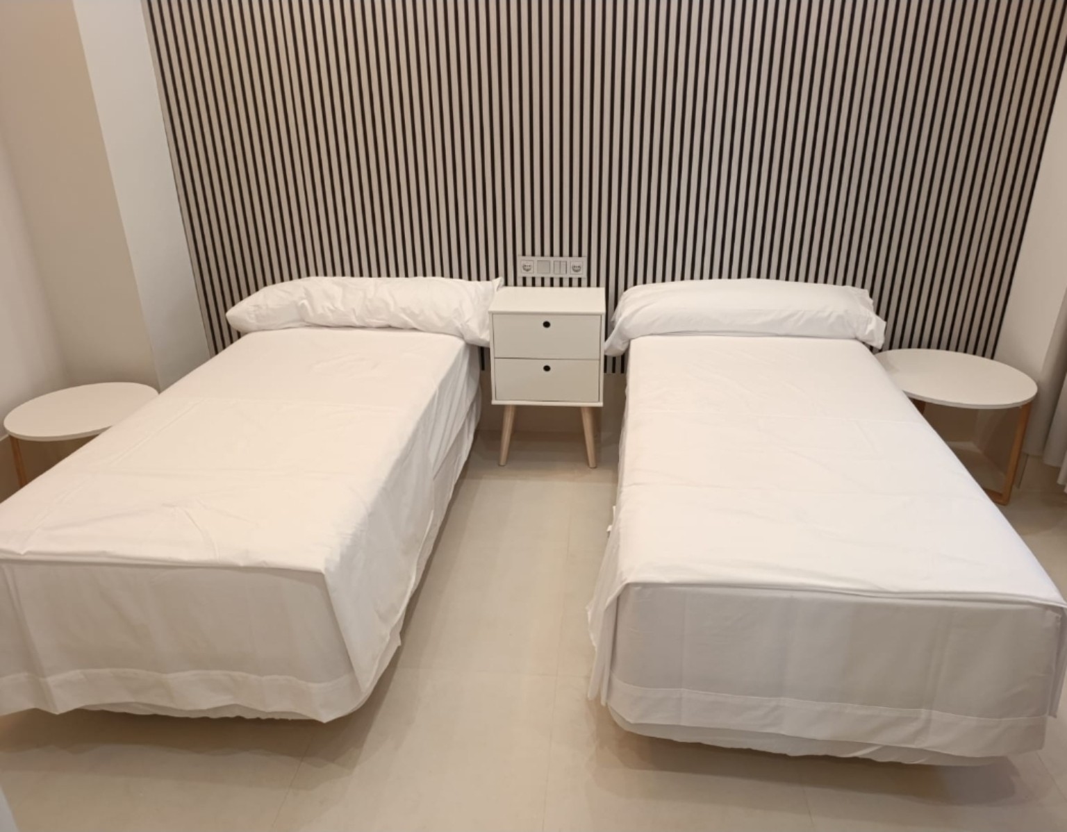Habitación de Hostal Tuhami con dos camas vestidas de blanco y cabecero de listones